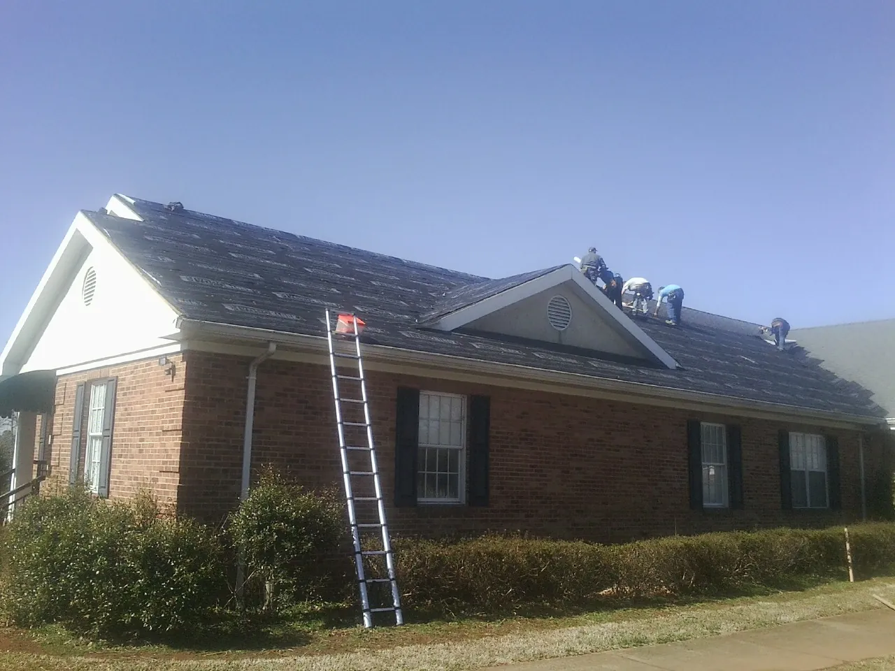 Crew tearing shingles off a brick ranch roof with a ladder set — Metal Roof Repair work by our crew in Cadogan