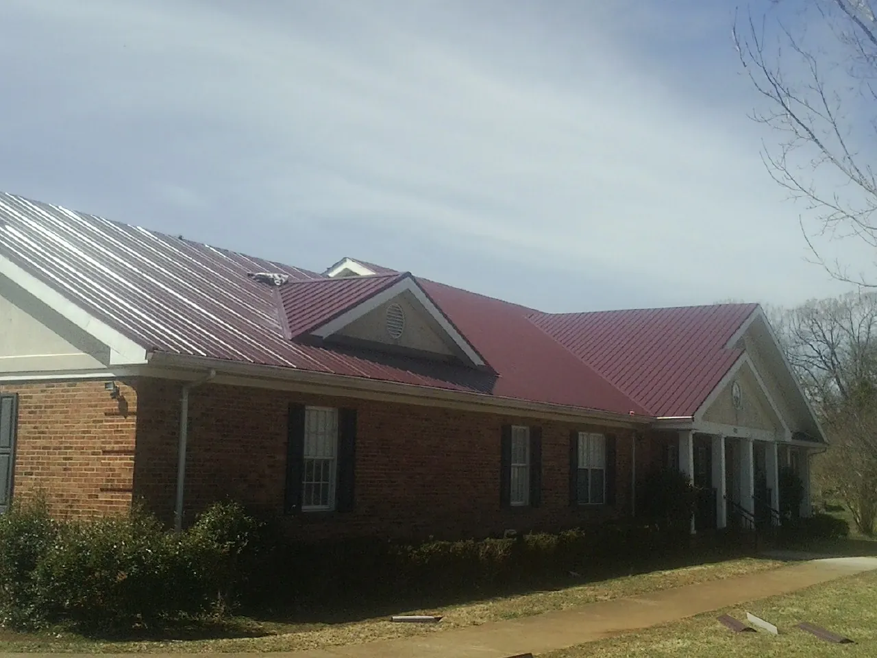 Red metal roof with gabled entries on a long brick building, from a Hail Damage Roof Repair job in Cadogan