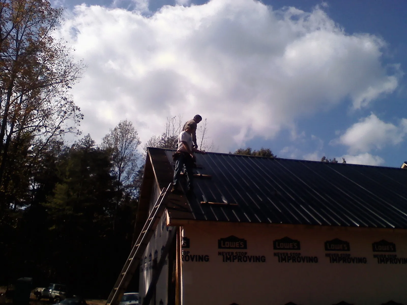 Roofer fastening dark metal panels high against a cloudy sky, from a Roof Inspection job in Cadogan
