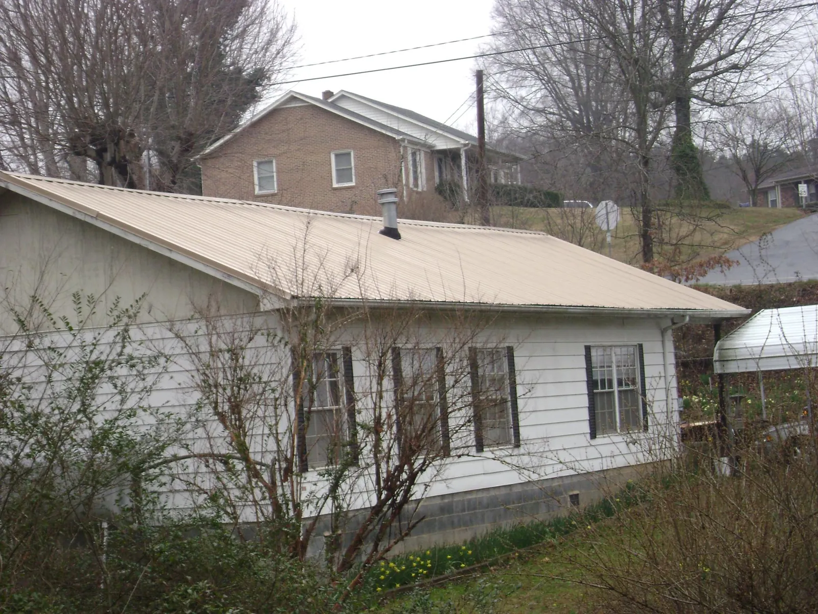 Tan metal roof on a white sided house set into a hillside — Commercial Roofing by Roofing Brothers in Cadogan