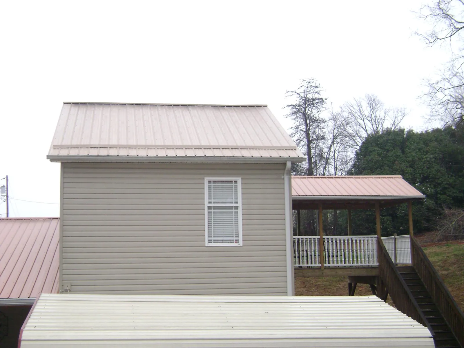 Tan metal roofs on a two story addition and attached porch, from a Roof Replacement job in Cadogan
